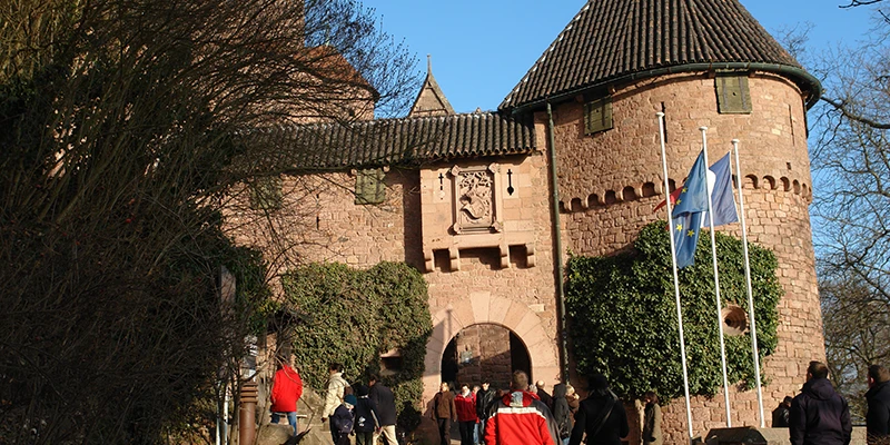 Visitors approaching the main entrance gate of Haut-Koenigsbourg beneath flags