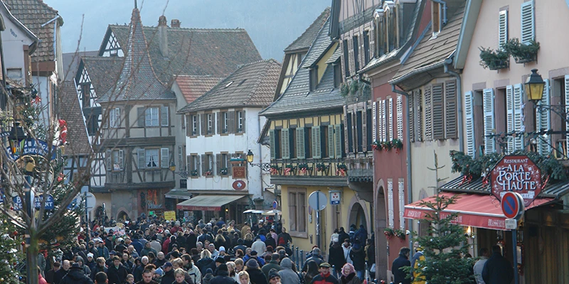 The main pedestrian street of Kaysersberg crowded with Christmas market visitors between half-timbered houses