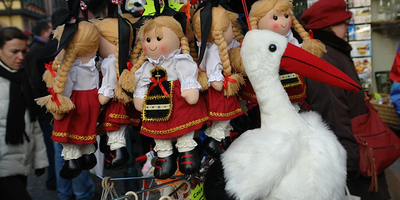 Market stall selling dolls in traditional Alsatian dress and stuffed white storks in Kaysersberg