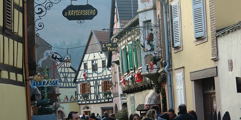Wrought-iron shop sign and painted houses at the entrance to Kaysersberg old town