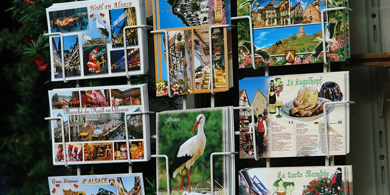 Postcard rack outside a shop in Kaysersberg showing Alsace scenes and storks