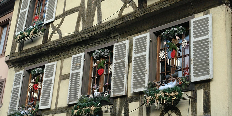 Christmas garlands and wreaths decorating the shuttered windows of a house in Kaysersberg