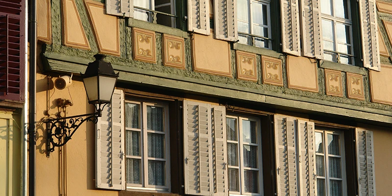 Yellow painted facade with shutters and a wrought-iron lamp in Ribeauvillé