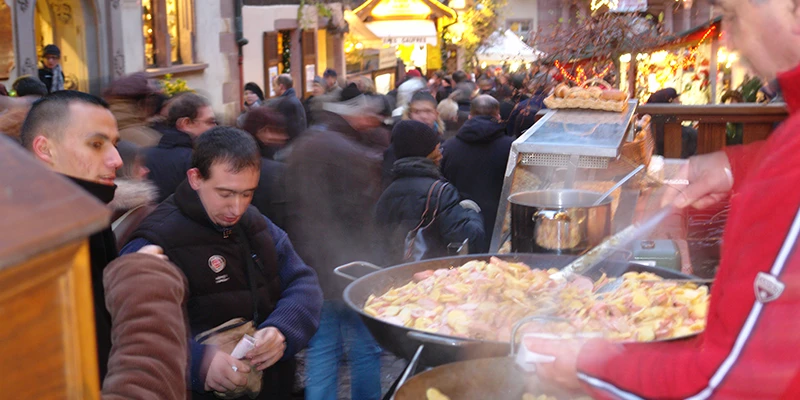 Vendor serving hot food from a large pan at the Riquewihr Christmas market