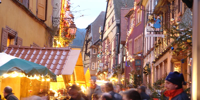 Market chalets and visitors along a decorated street in Riquewihr after dark