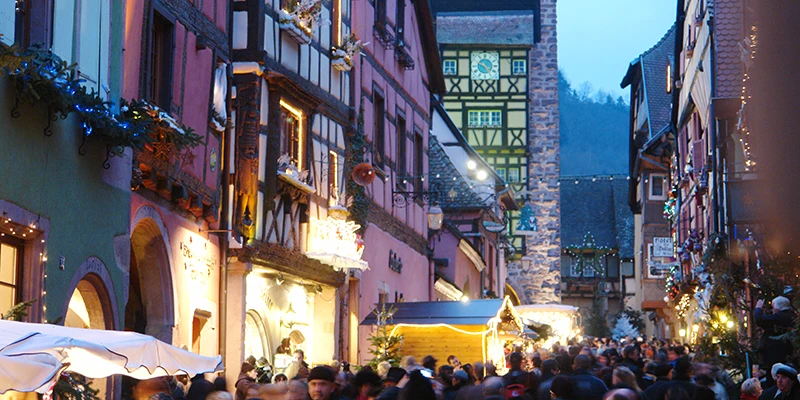 The main street of Riquewihr filled with Christmas market crowds at twilight