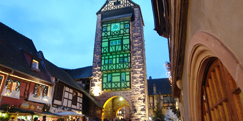 The Dolder tower in Riquewihr lit against a deep blue evening sky
