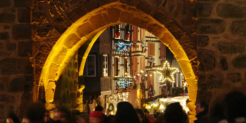 Illuminated stone gate arch in Riquewihr with the Christmas market beyond