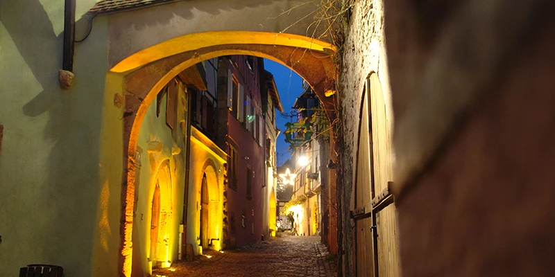 Lamplit cobbled lane running beneath an arch in Riquewihr