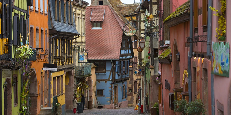Brightly painted facades in orange, blue and pink along a street in Riquewihr