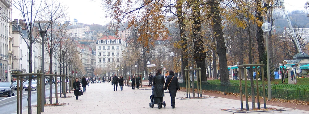 Wide pedestrian promenade in central Lyon lined with autumn trees