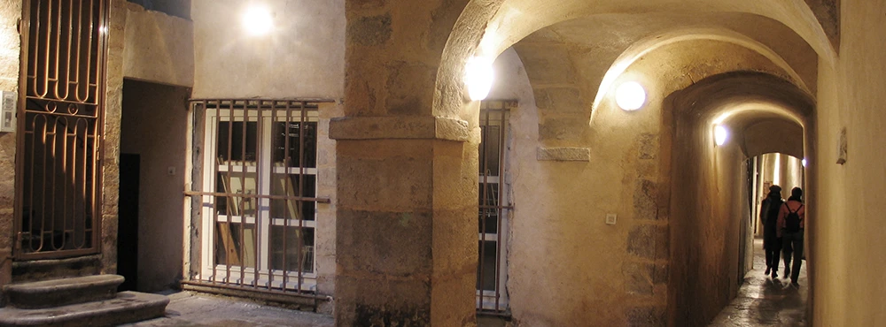 People walking through a long vaulted traboule passage in Lyon