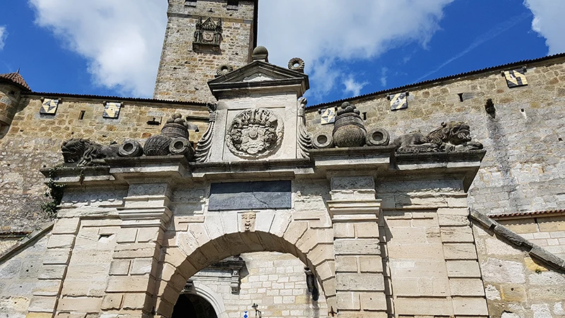 Stone gateway of the Veste Coburg with carved coats of arms above the arch against a blue sky