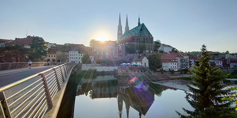 The Church of St. Peter and Paul in Görlitz rising above the riverside houses, its green copper roof and twin white spires prominent against a blue sky