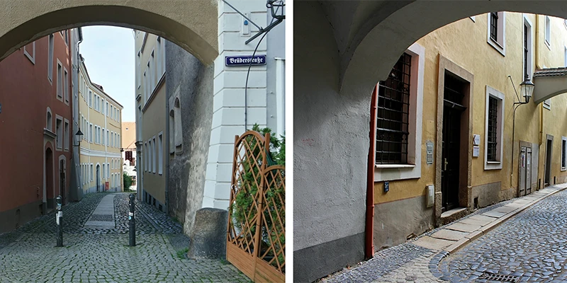 Sunlit Görlitz lane with ochre-yellow buildings, a stone archway overhead, a street lamp on the wall, and two people walking in the distance