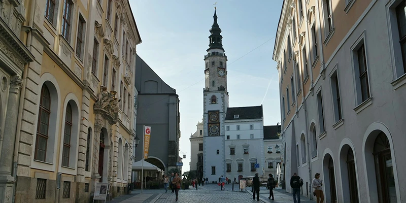 The Görlitz town hall tower with its clock and spire seen down a pedestrian street lined with historic facades and a few walkers