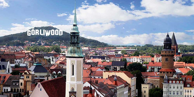 Aerial view over the red rooftops of Görlitz with a green church spire and several towers rising among the buildings, hills in the distance