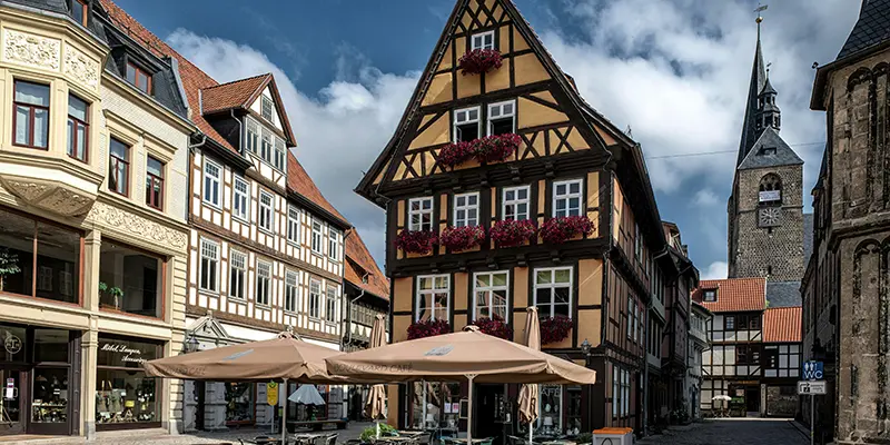 A market-square corner with a tall timber house, café umbrellas and a church tower