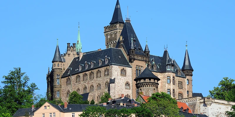 Schloss Wernigerode, a turreted castle on a wooded hill above the town, set against a clear blue sky