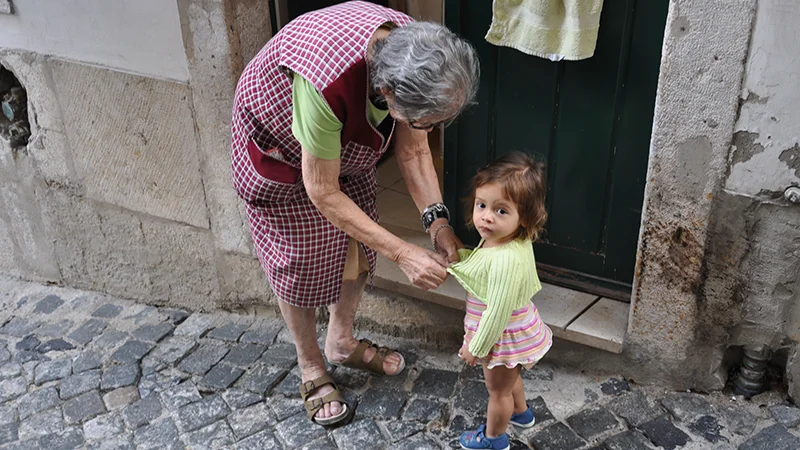 Grandmother helping a small child walk on the cobbles of an Alfama lane