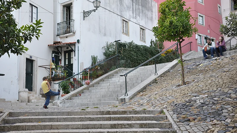 Staircase street descending between buildings and trees in Alfama