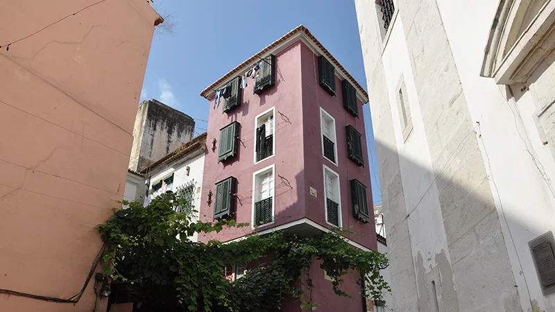 Pink and red painted building corner in Alfama against a blue sky