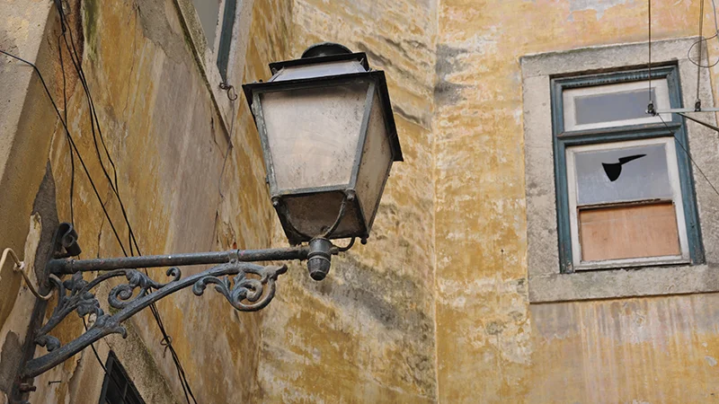 Ornate iron street lamp mounted on a yellow wall in Alfama