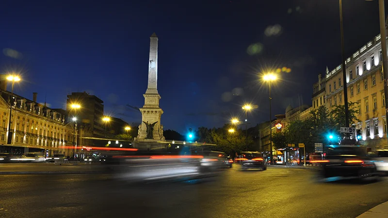 Night view of a Lisbon square with an illuminated column and traffic light trails