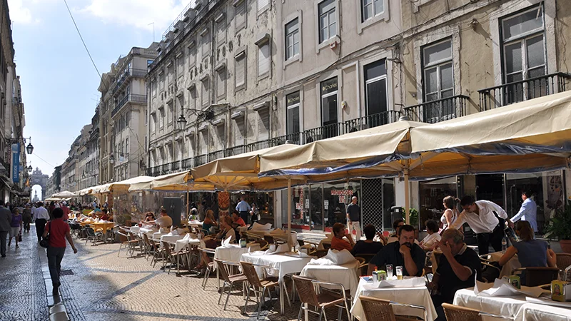 Wide Baixa street lined with cafe awnings and outdoor tables
