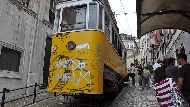 Yellow funicular car climbing a steep Lisbon street