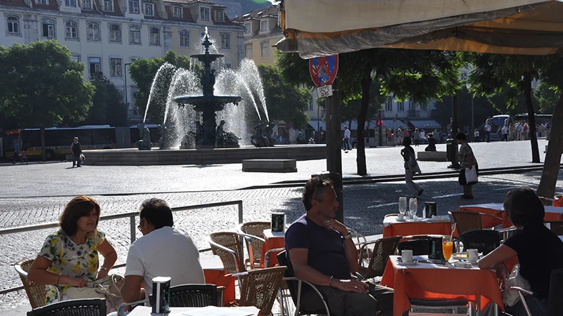 Outdoor cafe tables with people sitting in Rossio square