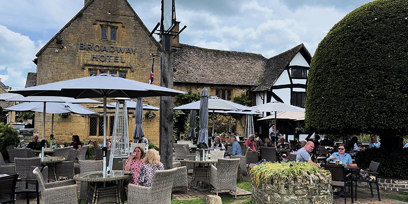 The Broadway Hotel with patrons at outdoor terrace tables, half-timbered wing visible to the side