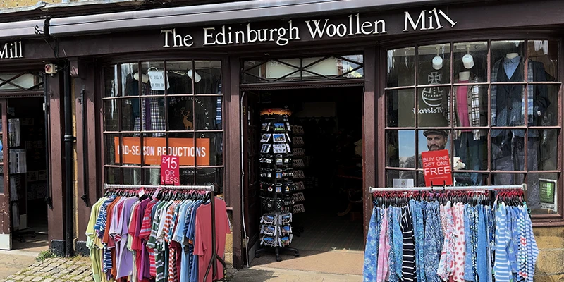 The Edinburgh Woollen Mill shop with clothing racks outside and mid-season reductions signs in window