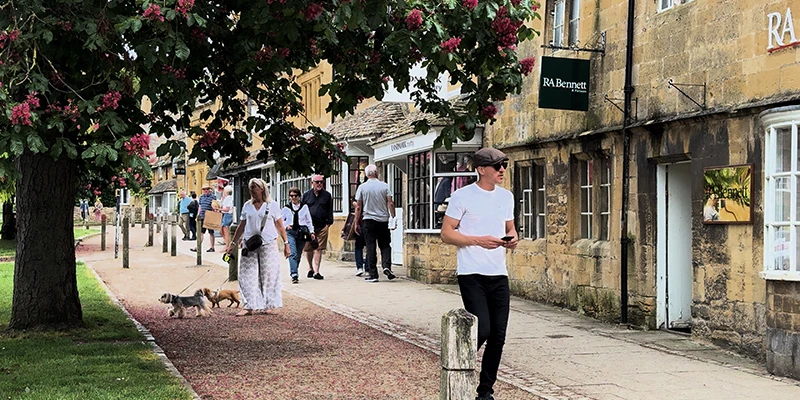 Visitors strolling along a tree-lined section of the High Street with shops to the right