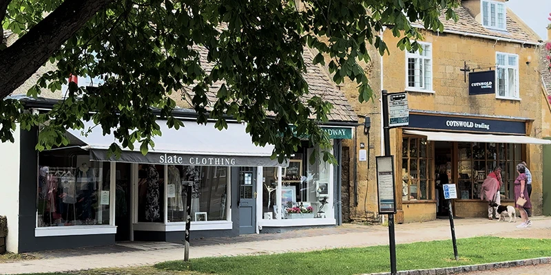 Slate Clothing and Cotswold Trading shops along Broadway High Street with mature chestnut tree overhead