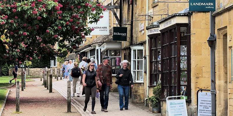 Visitors strolling past shops on Broadway High Street under tree-lined sidewalks