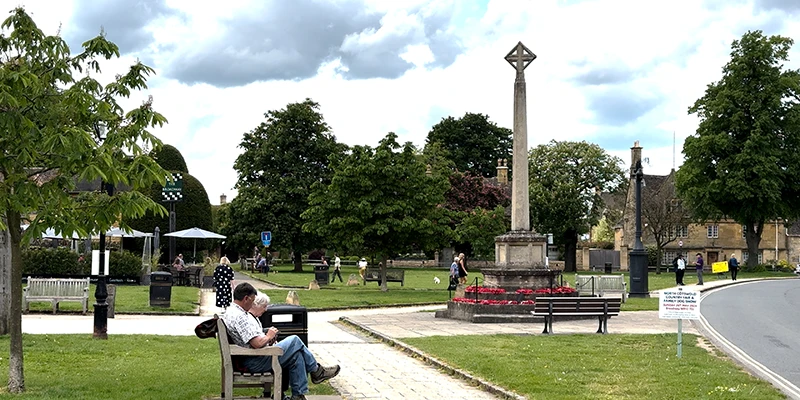The village green with its tall stone war memorial cross and benches under chestnut trees