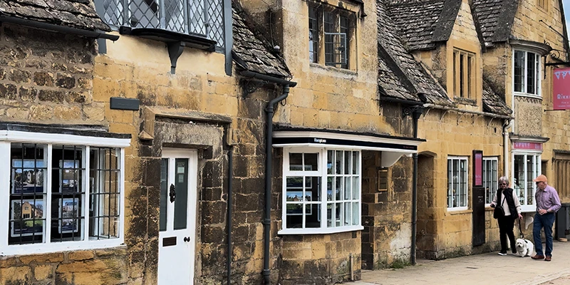 Honey-stone shops along Broadway High Street with bay windows and slate roofs