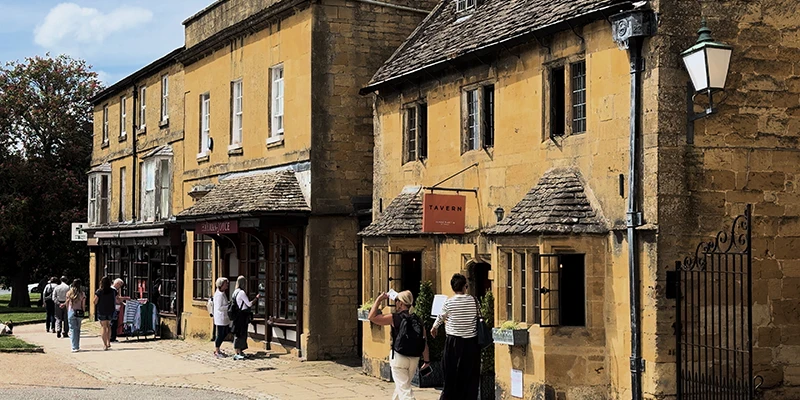 A row of classic Cotswold-stone shops with the Hayman-Joyce estate agent and Tavern signs