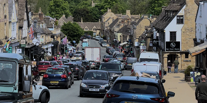 Busy traffic on Burford High Street with cars and vans backed up along the road