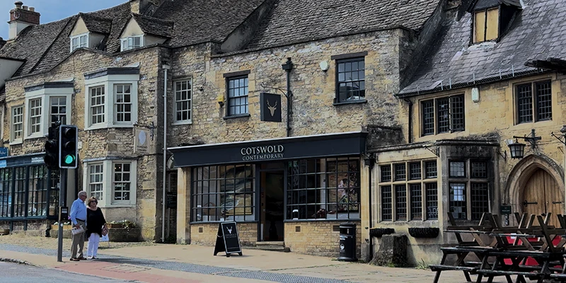 Wide view of Burford High Street with pedestrians along the row of stone shopfronts