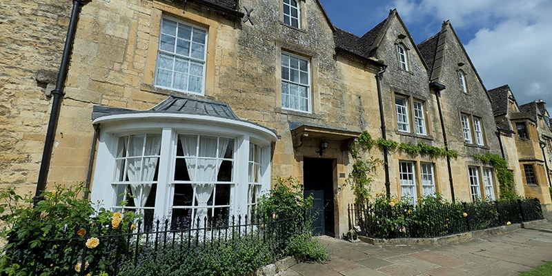 Cotswold-stone house with bay window and yellow roses