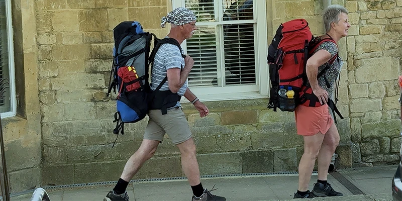 Two backpackers walking past a Cotswold stone wall