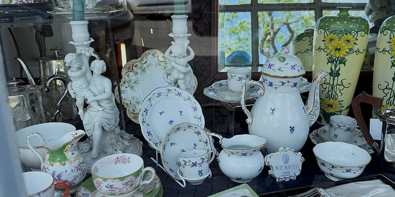 Antique window display with porcelain teapots, painted vases and silver