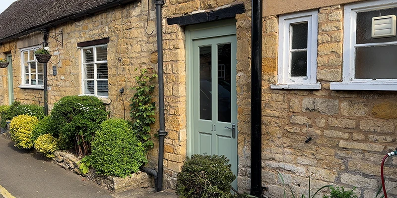 Honey-colored stone cottage with green door and climbing plants