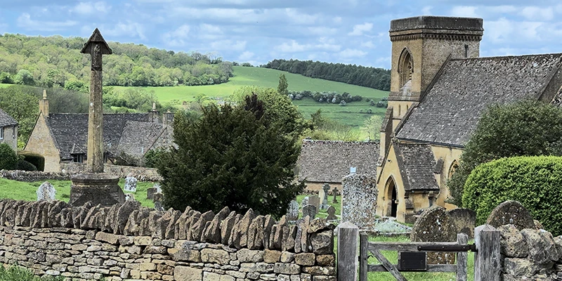 Village cross monument, churchyard, and dry-stone wall with hills in background