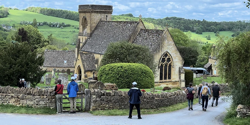 Visitors approaching St Barnabas Church along the village lane with rolling hills behind