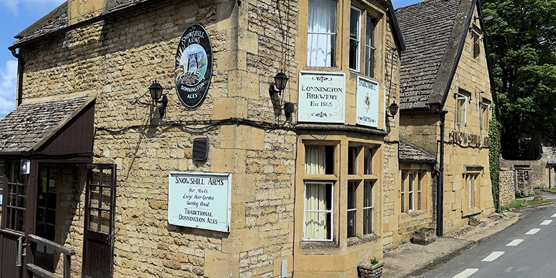 Close-up of the pub corner showing Donnington Brewery sign and Snowshill Arms board