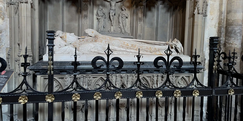 A carved stone tomb effigy behind iron railings in Ely Cathedral