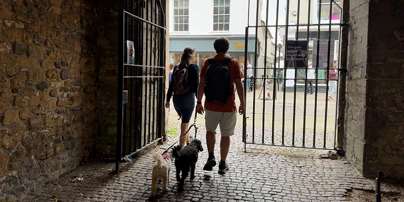 A couple walking a dog through the stone passage of the Porta gateway